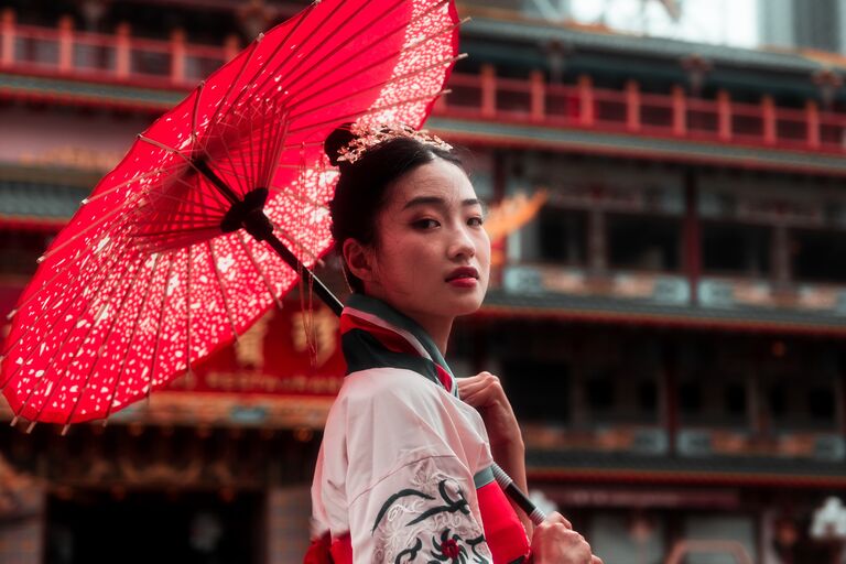Eine rot-weiß gekleidete Japanerin mit einem rotem Sonnenschirm